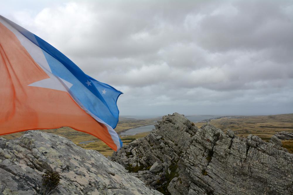 Bandera de la provincia de Tierra del Fuego, Antártida e Islas del Atlántico Sur  en lo más alto del Monte Tumbledown, de lejos Puerto Argentino (Islas Malvinas). En memoria de nuestros soldados.